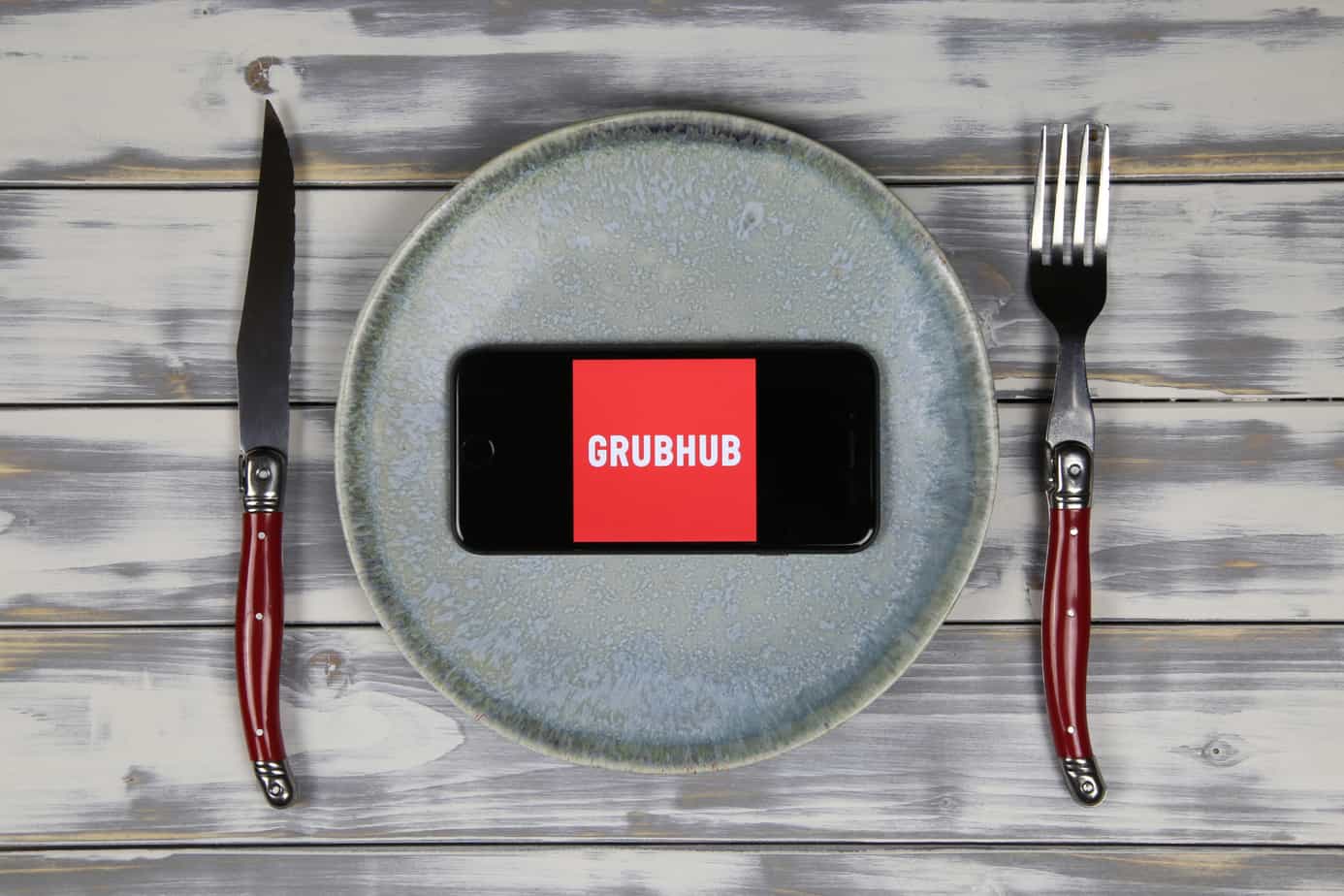 close up of mobile phone screen with logo lettering of food delivery service grubhub on wood table with dish and cutlery 205467998 close up of mobile phone screen with logo lettering of food delivery service grubhub on wood table with dish and cutlery 205467998