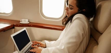Businesswoman using a laptop on private jet for payment processing and merchant services.