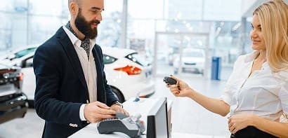 Mobile payment transaction at car dealership with friendly staff.