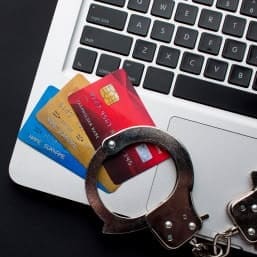 Secure payment cards and handcuffs on laptop keyboard, illustrating merchant payment security.