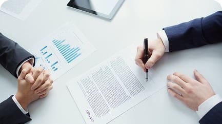 Business professionals signing a contract with financial charts on the desk, representing merchant services agreement.