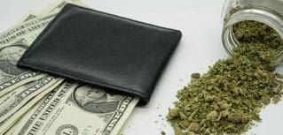 Black wallet on cash and cannabis buds, financial and legal considerations.