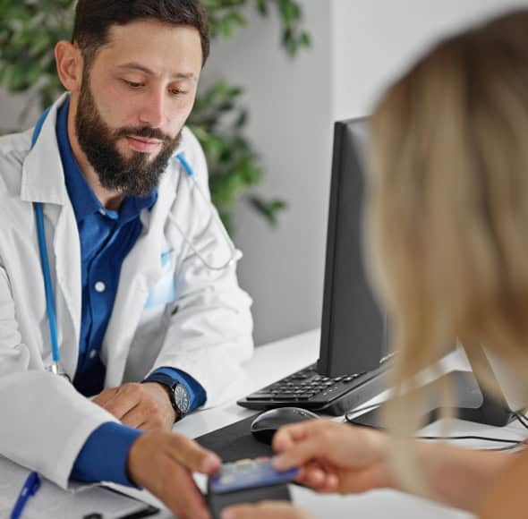 Doctor in white coat assisting a patient with payment processing at clinic, emphasizing healthcare merchant services.