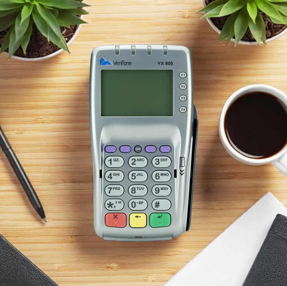 Portable credit card terminal on wooden desk with plants and coffee, ideal for secure payment processing.