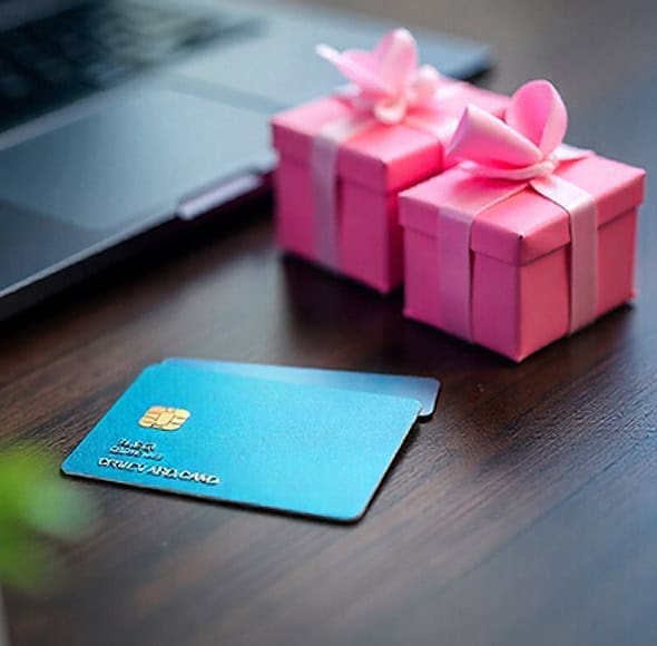 Plastic credit card on wooden table with pink gift boxes, digital payment, online shopping, Host Merchant Services collaboration.