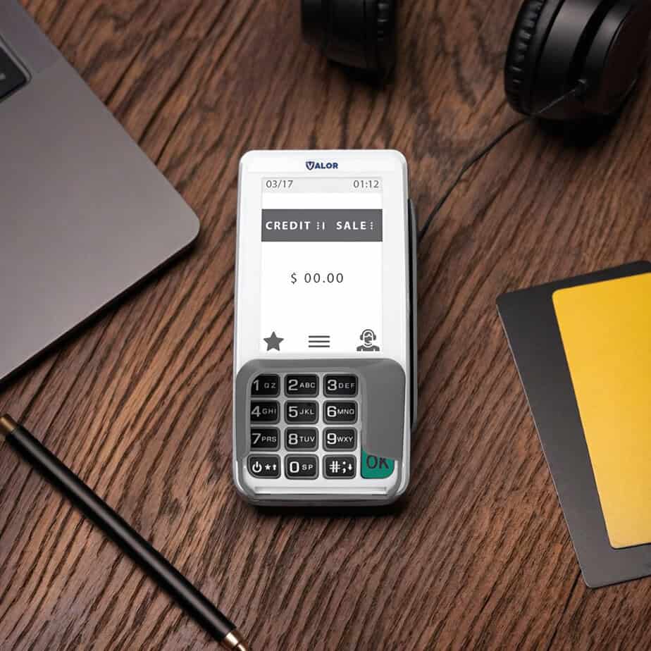 Mobile credit card reader for Host Merchant Services on wooden desk with accessories.